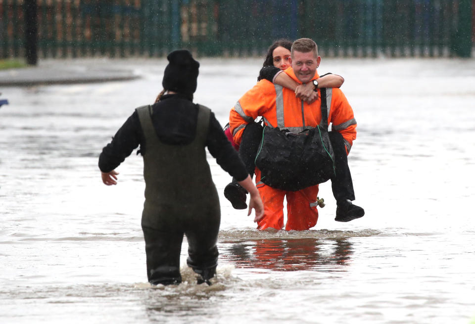 A man in high visibility overalls carries a woman through floodwater in Doncaster, Yorkshire, as parts of England endured a month's worth of rain in 24 hours (PA)