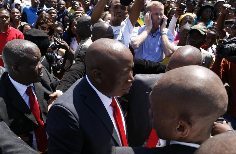 Firebrand politician Julius Malema, center, is escorted by his bodyguards to address supporters after appearing at the Magistrate’s Court in Polokwane, South Africa, Wednesday, Sept. 26, 2012, on charges of money laundering in connection with an improper government tender awarded to a company his family trust partly owns. (AP Photo/Themba Hadebe)