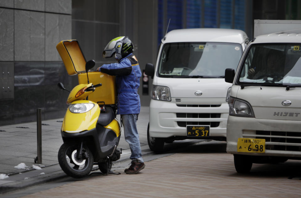In this Thursday, Feb. 13, 2014 photo, a motorcycle messenger prepares for another delivery in the business district in Tokyo. Over the past two decades Japan’s system of salaried jobs with full benefits has crumbled companies struggled to stay afloat in cut-throat global markets. The salaried steady jobs in manufacturing and finance that have moved abroad or become obsolete are being replaced by low-paying service jobs such as clerking in convenience stores and delivery work, especially for workers under age 40. (AP Photo/Junji Kurokawa)