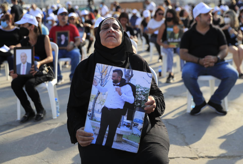 The mother of a victim who was killed in the massive blast last year at the Beirut port holds a portrait of her son as she attends a Mass held to commemorate the first year anniversary of the deadly blast, at the Beirut port, Lebanon, Wednesday, Aug. 4, 2021. United in grief and anger, families of the victims and other Lebanese came out into the streets of Beirut on Wednesday to demand accountability as banks, businesses and government offices shuttered to mark one year since the horrific explosion. (AP Photo/Hussein Malla)