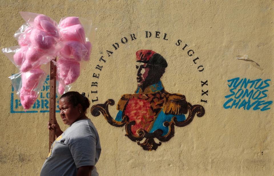 A cotton candy vendor stands next to a mural of Venezuela's late President Hugo Chavez as she watches a gathering between President Nicolas Maduro and students in Caracas, Venezuela, Saturday, March 22, 2014. Two more people were reported dead in Venezuela as a result of anti-government protests even as supporters and opponents of Maduro took to the streets on Saturday in new shows of force. (AP Photo/Esteban Felix)