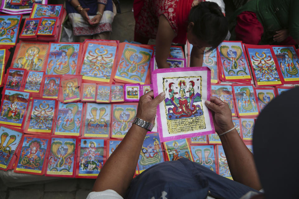 In this Aug. 4, 2019, photo, a Nepalese man checks a traditional painting displayed for sale at a market during Naag Panchami festival in Bhaktapur, Nepal. The art and tradition of Nepal’s Chitrakar families, who depicted gods and goddesses on temples, masks of Hindu deities and posters for various religious celebrations is dying because of mass machine printed posters and card-size pictures of gods that are cheaper and more popular. (AP Photo/Niranjan Shrestha)