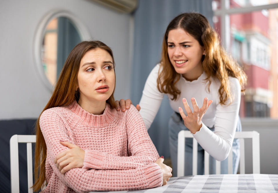 Woman sitting down crying while angry woman yells and gestures at her