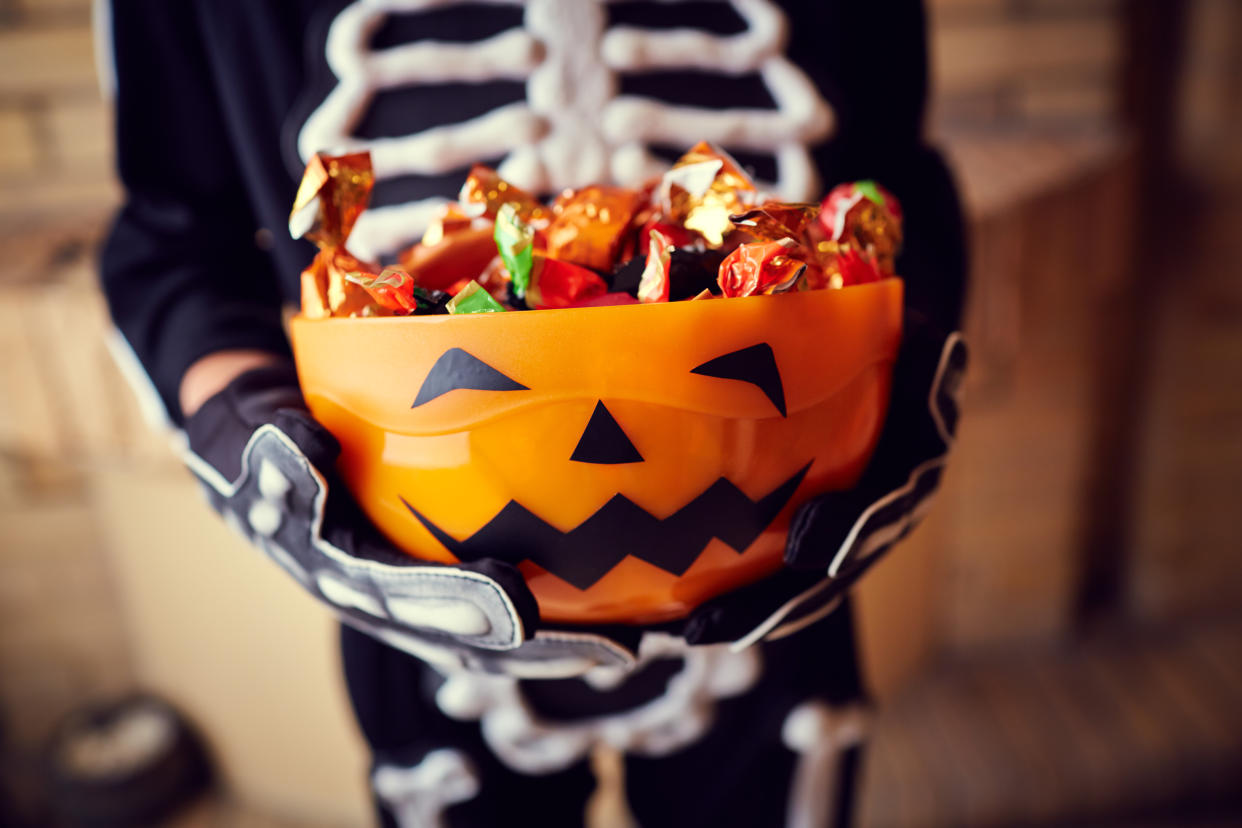 Boy in skeleton costume holding bowl full of candies for Halloween