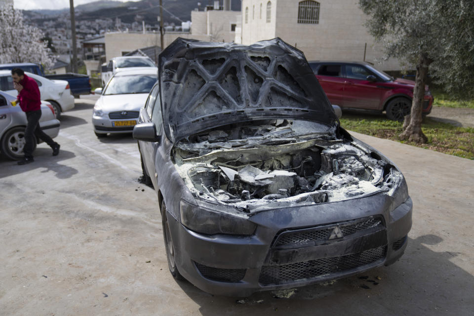 A man walks past a vehicle allegedly set ablaze by Jewish West Bank settlers in the Palestinian West Bank village of Turmus Ayya, Sunday, Feb. 18, 2024. Village residents claimed that settlers raided the outskirts of the village overnight, setting fire to a car and spaying graffiti on the walls of homes. (AP Photo/Nasser Nasser)