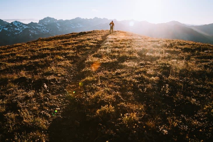 A lone hiker on a high ridge with a stunning sunset vista of the Olympic mountain range. Shot in Washington state on the Olympic Peninsula