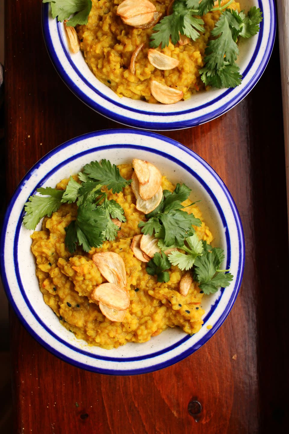 a bowl of turmeric yellow khichdi in a blue rimmed bowl with fried garlic chips and green cilantro