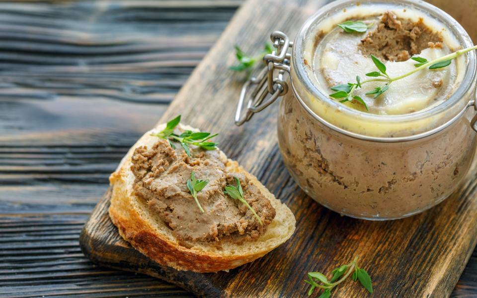 Homemade beef liver pate in a glass jar and baguette slices with pate on the serving board, selective focus.