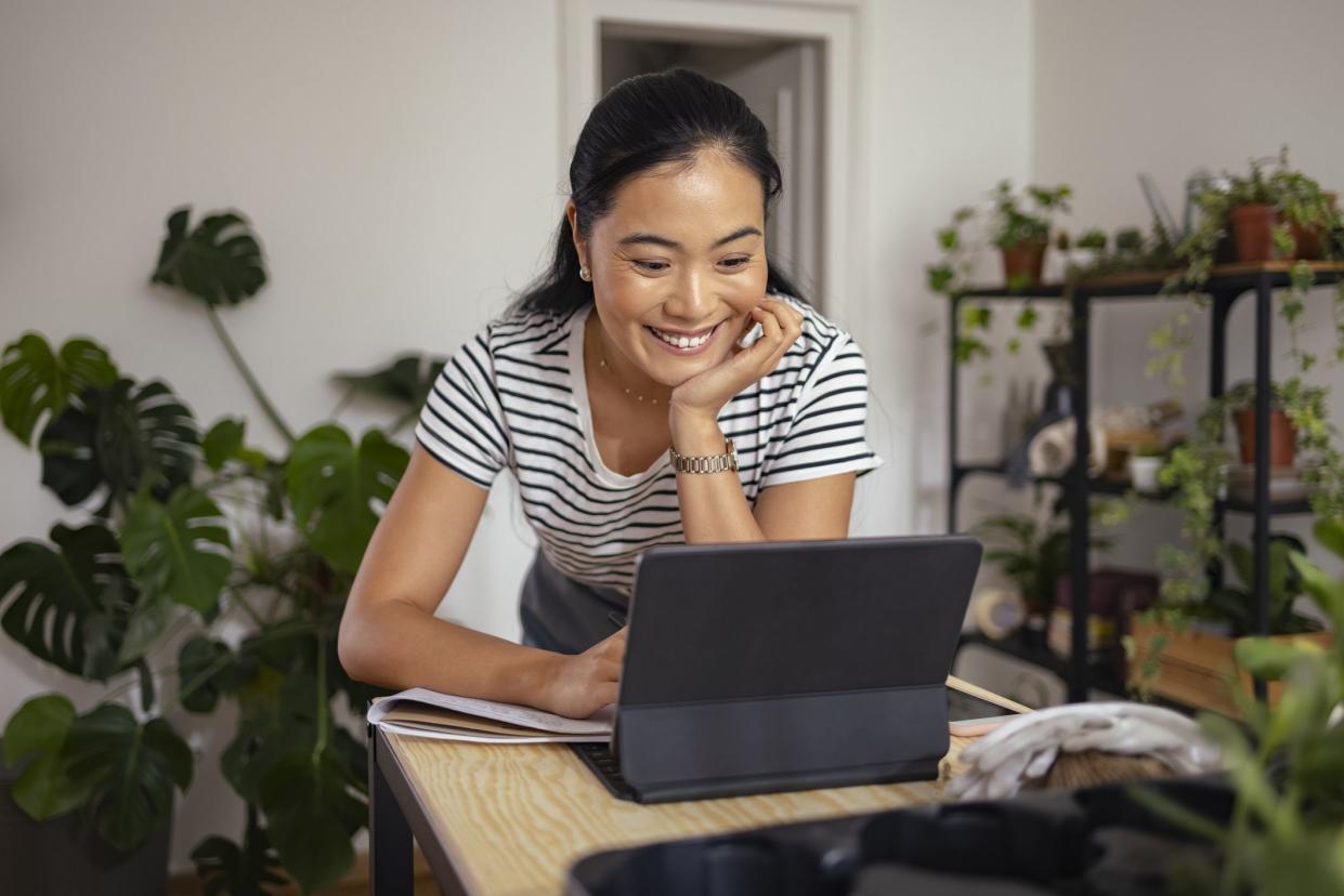 Smiling Asian woman talking with client on online video call meeting while standing in her workshop.