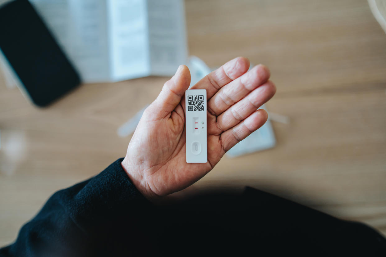 Overhead view of senior vegan Asian woman carrying out a Covid-19 rapid lateral flow test at home. She is holding a positive Coronavirus rapid self test device, feeling worried