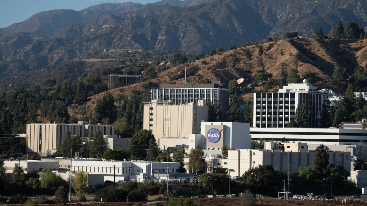  A handful of white and tan buildings, one with a large blue nasa logo, sit in the foothills of mountains. 