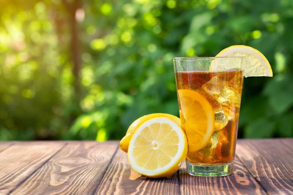 glass of ice tea with lemon on wooden table outdoors