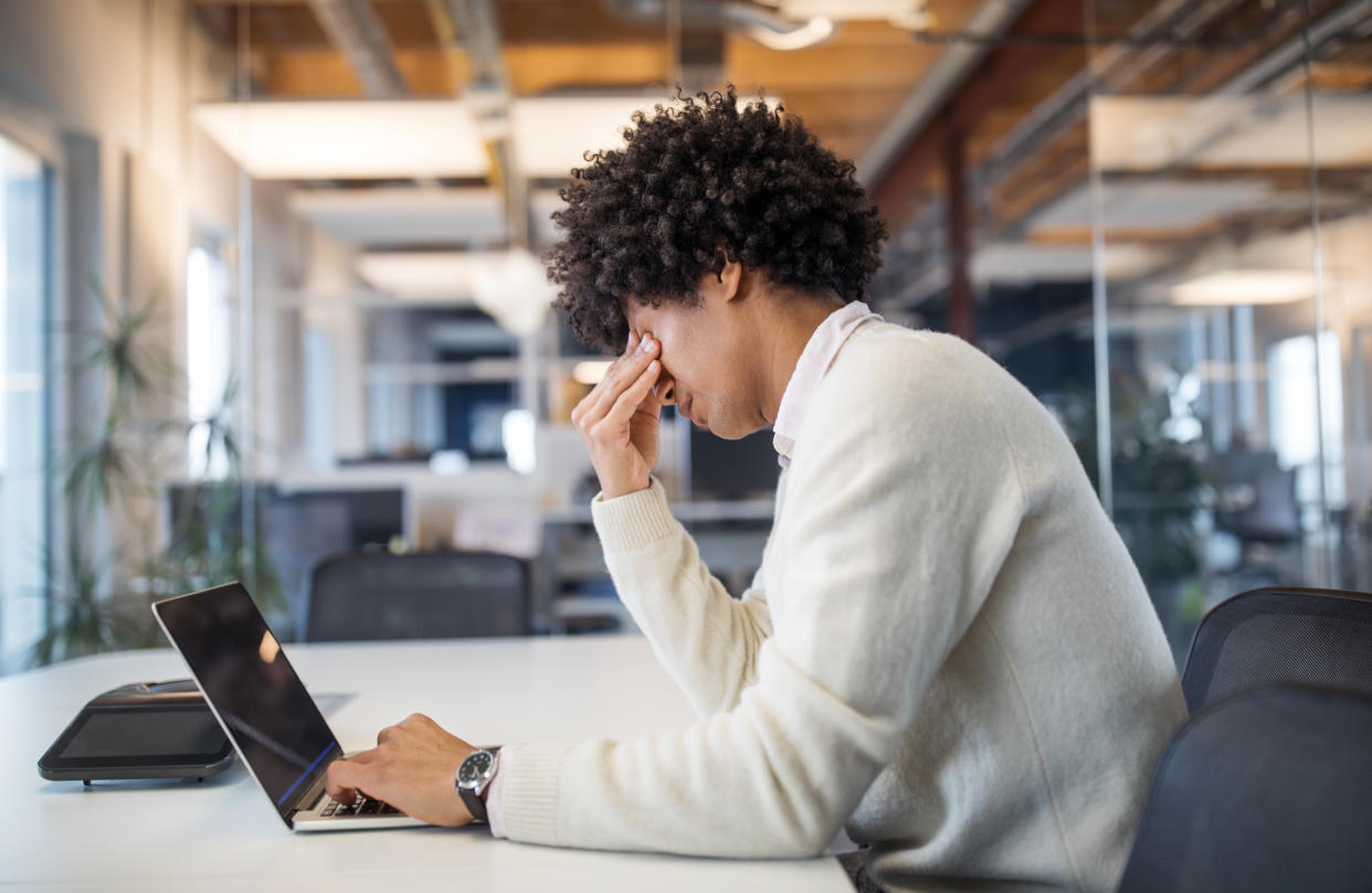 Young businessman working late in office looking stressed. Male professional feeling tired while working on laptop in modern office.