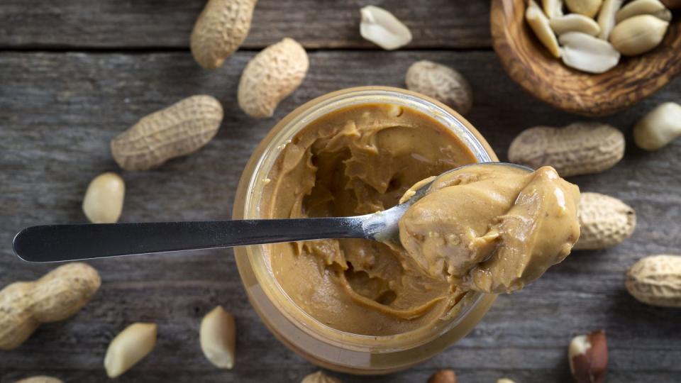spoon and pot of peanut butter on wooden background