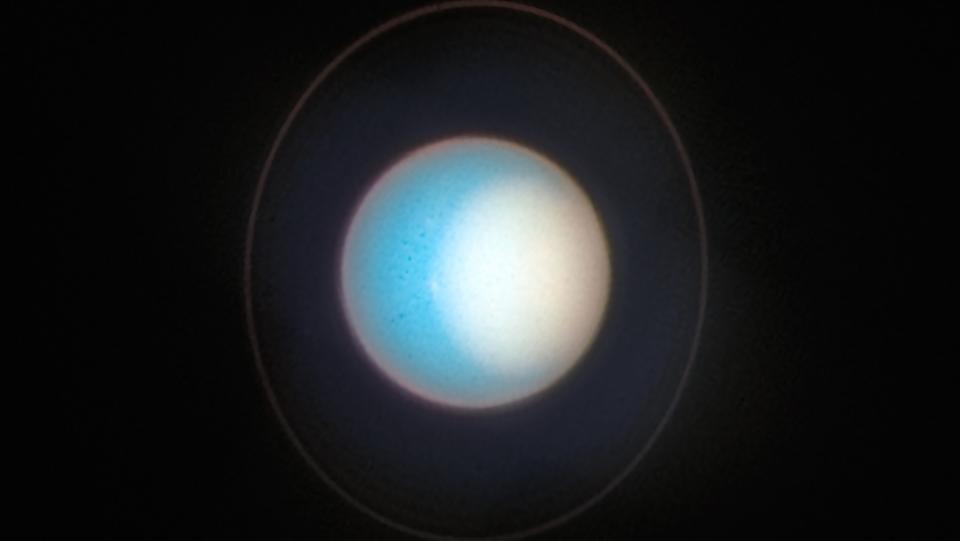 hubble telescope image of the blue planet uranus with a white polar cap and rings visible.