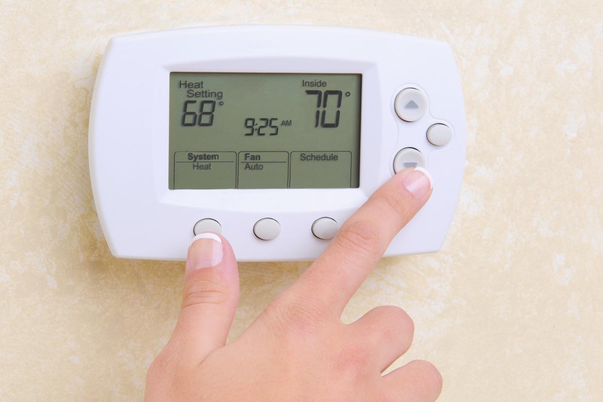 woman's hand setting the room temperature on a programmable thermostat