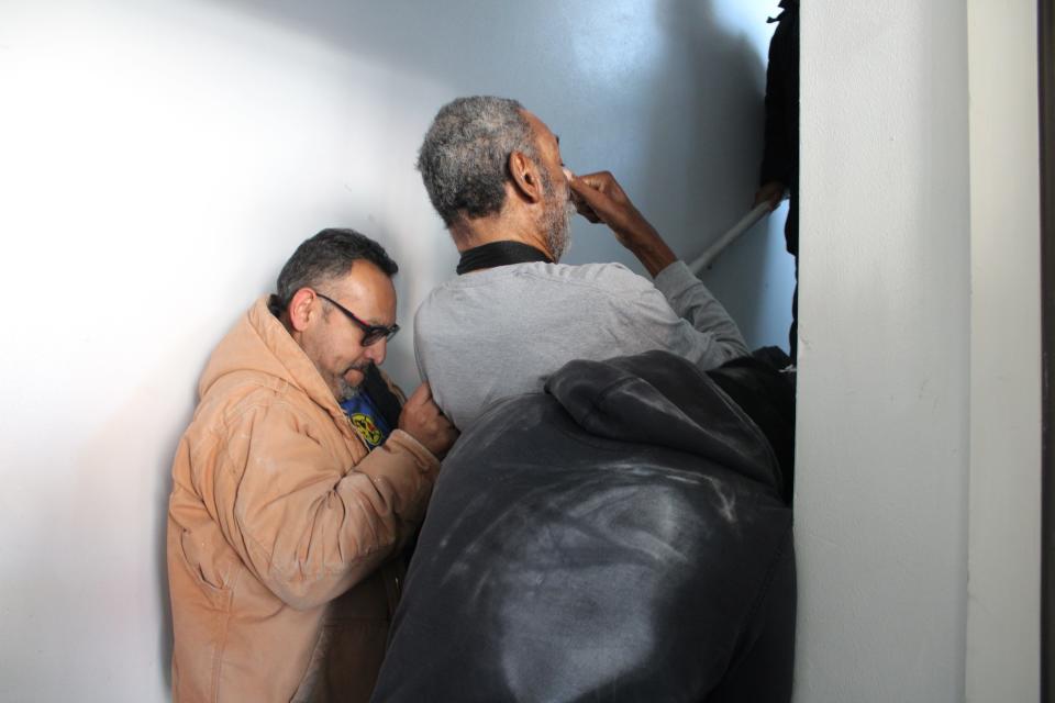 Two men assist in carrying Jewel Currie down the stairs of his building before an appointment.