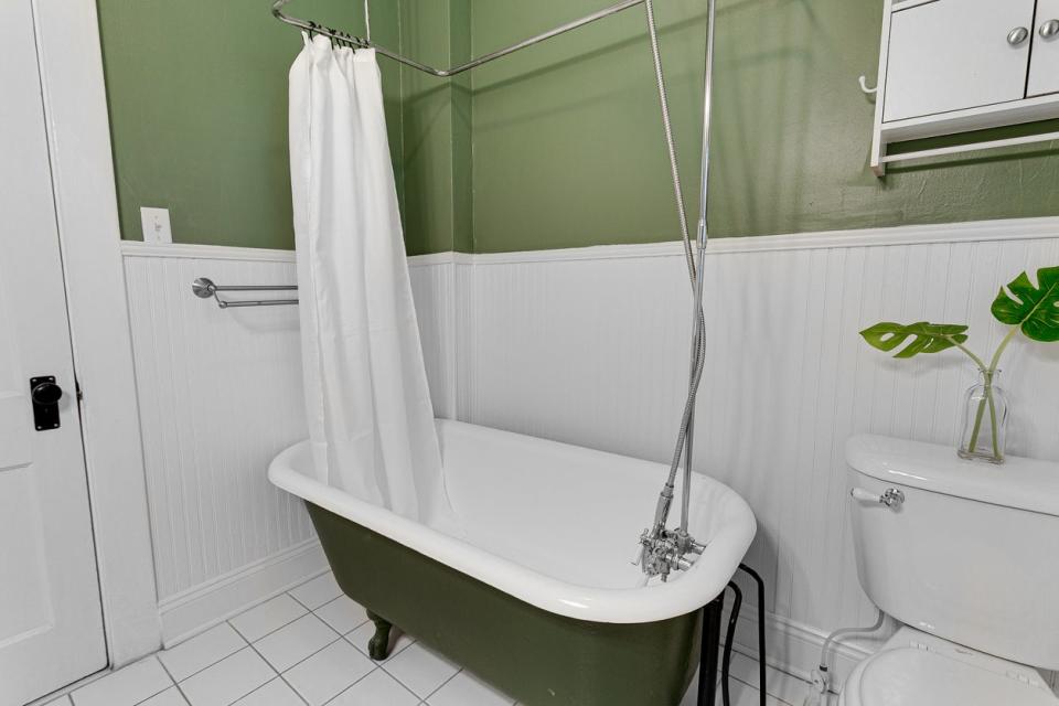 Simple bathroom with green walls, white claw foot bathtub, shower curtain, and wainscoting.