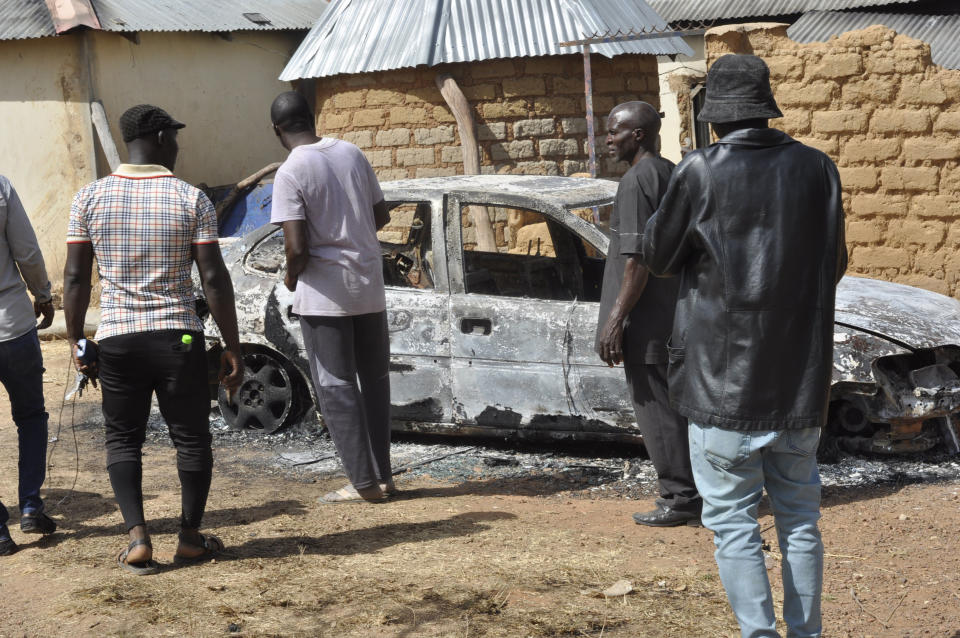 People stand by a burnt out car following an attacked by gunmen in Bokkos, north central Nigeria, Tuesday, Dec. 26, 2023. Nigerian officials and survivors say at least 140 people were killed by gunmen who attacked remote villages in north-central Nigeria's Plateau state in the latest of such mass killings this year blamed on the West African nation's farmer-herder crisis. (AP Photo)