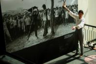 A TV reporter speaks in front of a picture at an exhibition on the 44th anniversary of a massacre of pro-democracy students by state forces at Thammasat University in Bangkok