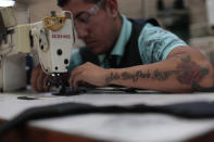 In this Feb. 13, 2020 photo, an employee, donning a tattoo with a motto reads in Spanish: "Only God can judge me," stitches shoe components at the Tenis Court factory, in Leon, Guanajuato state, Mexico. Part of Guanajuato’s odd reality stems from its success at cracking down on crimes that impact businesses together with its inability to stop the drug gang war. (AP Photo/Rebecca Blackwell)