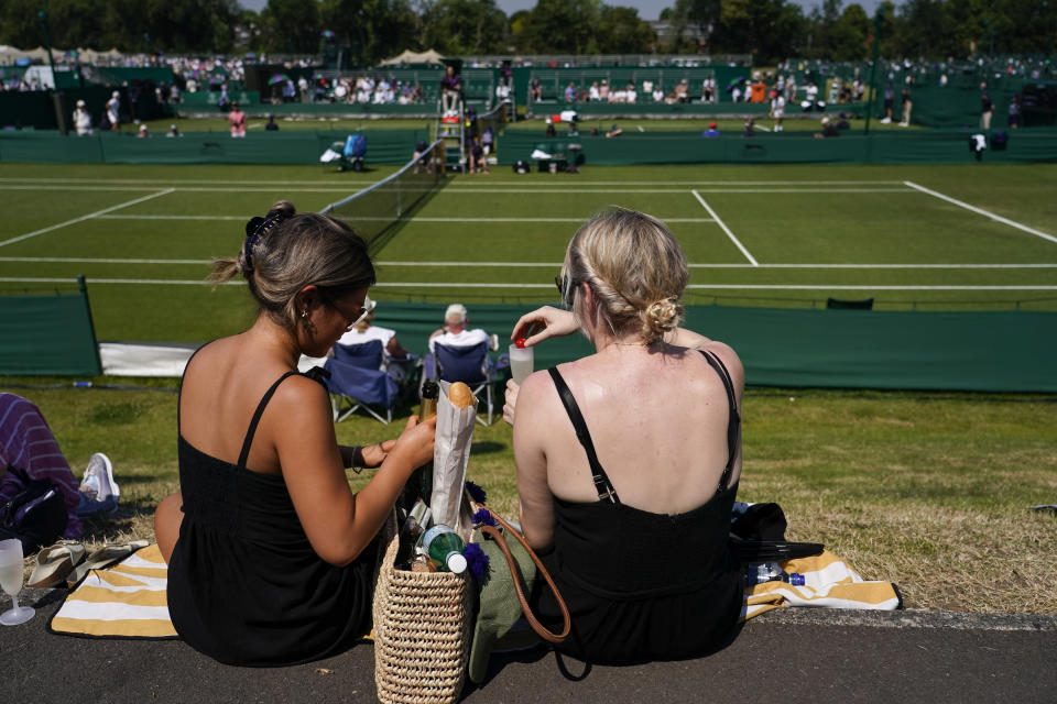 Spectators have a drink as they sit on the grass at the Roehampton Community Sports Centre in Roehampton, London, Wednesday, June 26, 2024, during Wimbledon qualifying. (AP Photo/Alberto Pezzali)