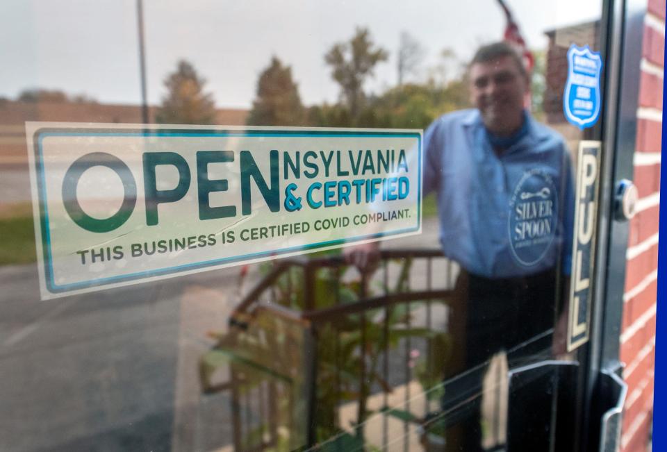 David LeHeron, the owner of the Blue Heron, reflects in the window displaying his Certified COVID Compliant sign on the main entrance of the Springettsbury Township, Pennsylvania, restaurant.