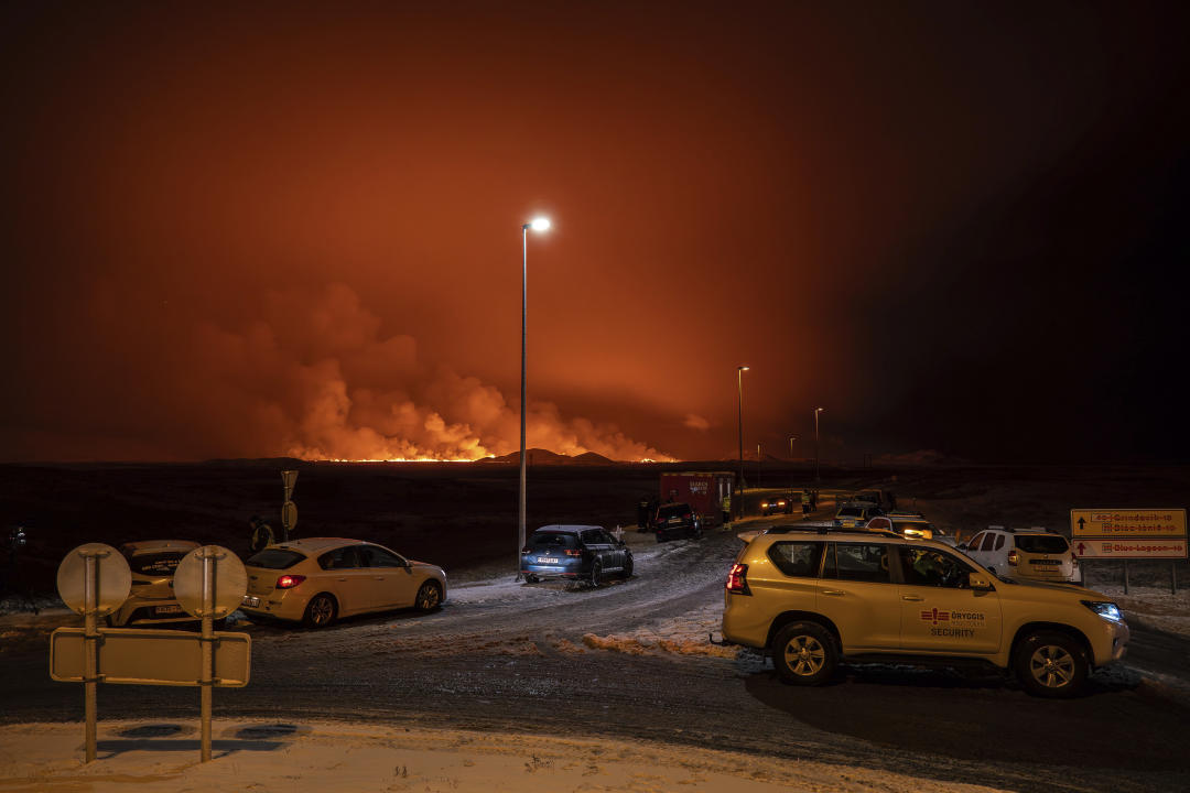 The road is blocked at the entrance of the road to Grindavík with the eruption in the background, in Grindavik on Iceland's Reykjanes Peninsula, Monday, Dec. 18, 2023. A volcanic eruption started Monday night on Iceland’s Reykjanes Peninsula, turning the sky orange and prompting the country’s civil defense to be on high alert. (AP Photo/Marco Di Marco)
