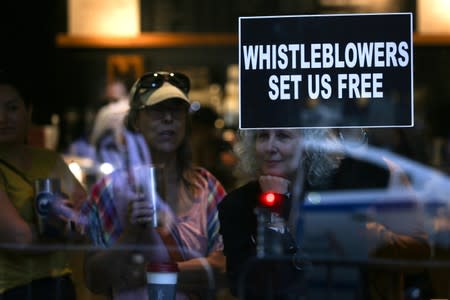 A woman holds a sign about whistleblowers in a cafe near U.S. President Trump’s motorcade as he attends a campaign fundraiser nearby in New York