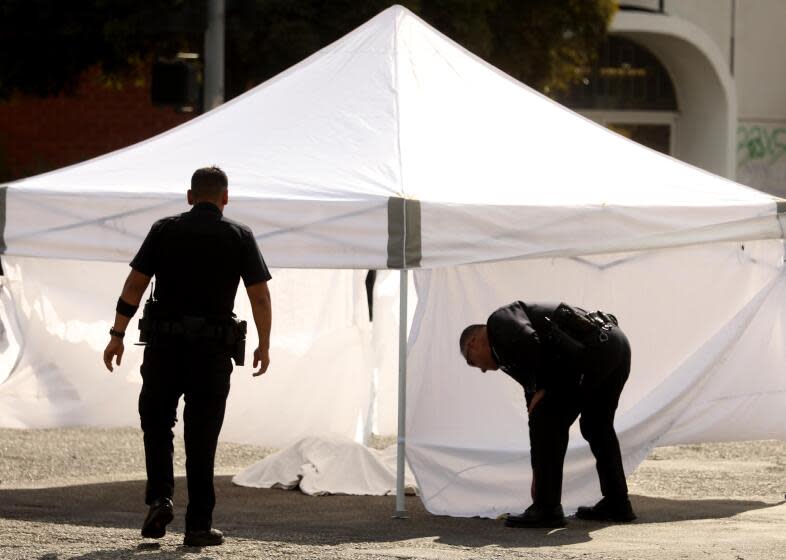 SOUTH LOS ANGELES, CA - OCTOBER 24, 2023 - A police officer monitors the scene where a person was killed in a hit-and-run while another officer tries and secures the tent surrounding the victim at the intersection of Broadway and El Segundo Blvd. in South Los Angeles on October 24, 2023. The motorist was being sought. Officers went to the area of South Broadway and West 117th Street at about 9:15 a.m., according to the Los Angeles Police Department. The fatally injured person, described only as a male, died at the scene, police said. Information on his identity was not immediately available. The hit-and-run vehicle was described as a white Chevrolet van. According to reports from the scene, the victim was dragged for some distance by the vehicle, and he might have been hit intentionally. (Genaro Molina / Los Angeles Times)