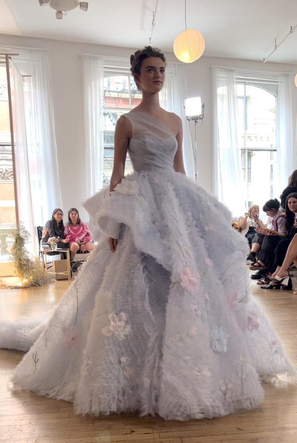 A woman walks down a runway in a blue wedding dress.