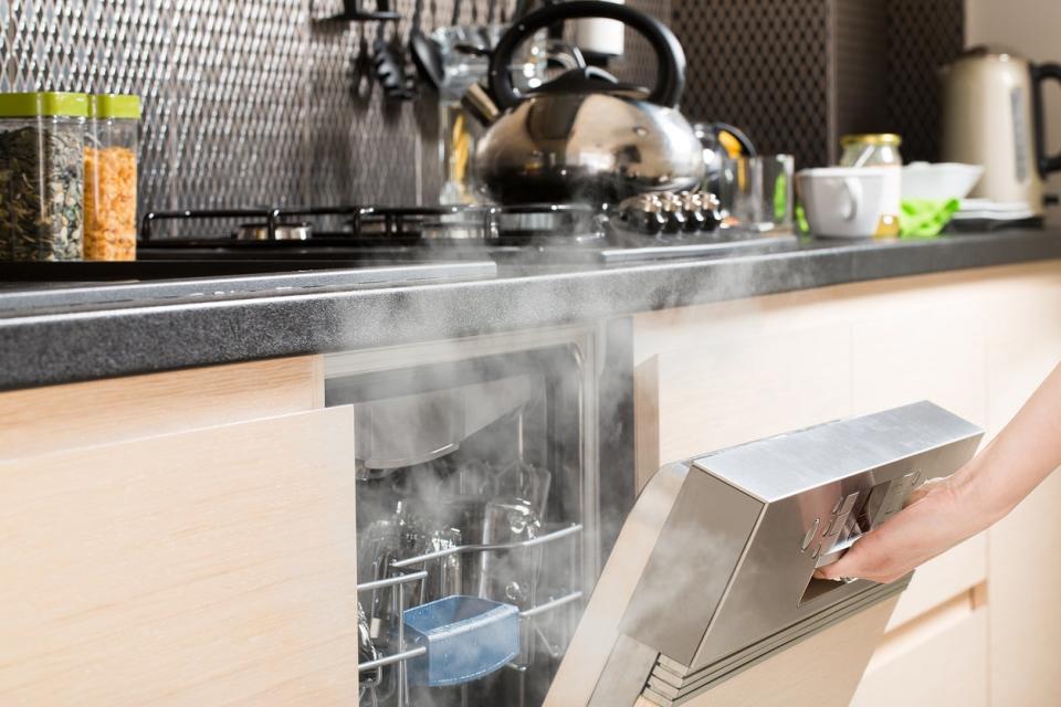 Dishwasher being opened after a hot wash cycle, letting steam out into a kitchen