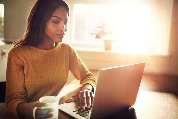 Woman holding mug using laptop