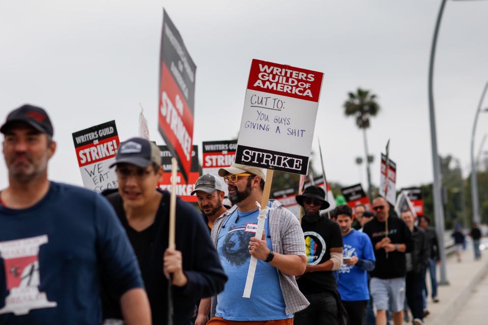 A supporter of the Writers Guild of America strike walks with a sign that reads, "Cut to: You guys giving a shit," as people picket along Colfax Avenue, at Radford Studios Center, in Studio City, CA, Tuesday, May 9, 2023.