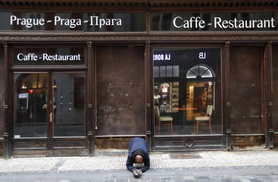 FILE - In this Sunday, Oct. 11, 2020 file photo, a beggar kneels in front of a closed restaurant in downtown Prague, Czech Republic. The coronavirus pandemic is gathering strength again in Europe and, with winter coming, its restaurant industry is struggling. The spring lockdowns were already devastating for many, and now a new set restrictions is dealing a second blow. Some governments have ordered restaurants closed; others have imposed restrictions curtailing how they operate. (AP Photo/Petr David Josek, File)