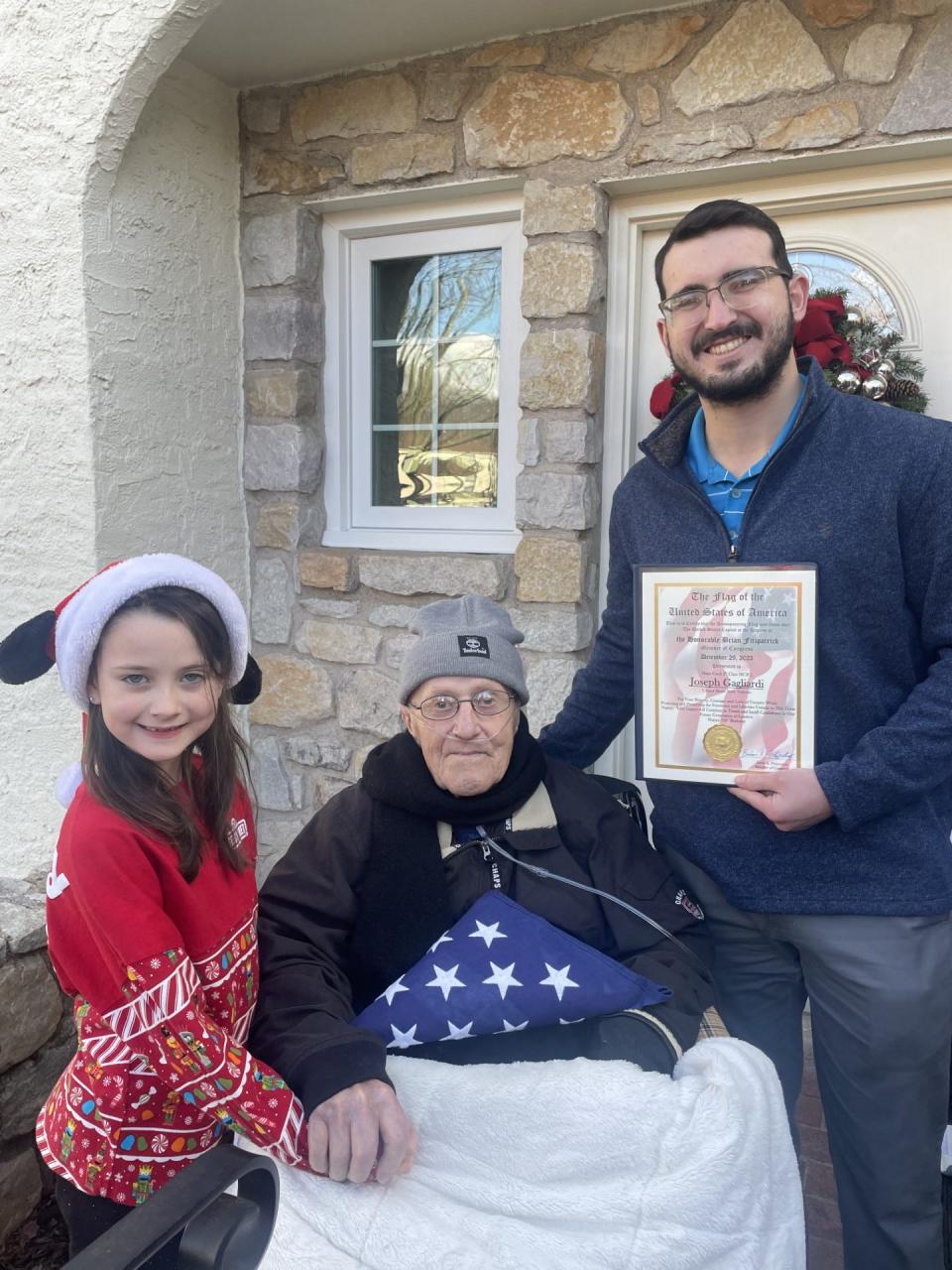 Centenarian Joseph Gagliardi of Newtown Township, a World War II veteran, accepts an American flag and proclamation from Brendan McCusker, a constituent advocate for Congressman Brian Fitzpatrick, as Layla Leuthy Peck, 7, watches. Layla also presented the veteran with 100 birthday cards to mark his special birthday Friday.