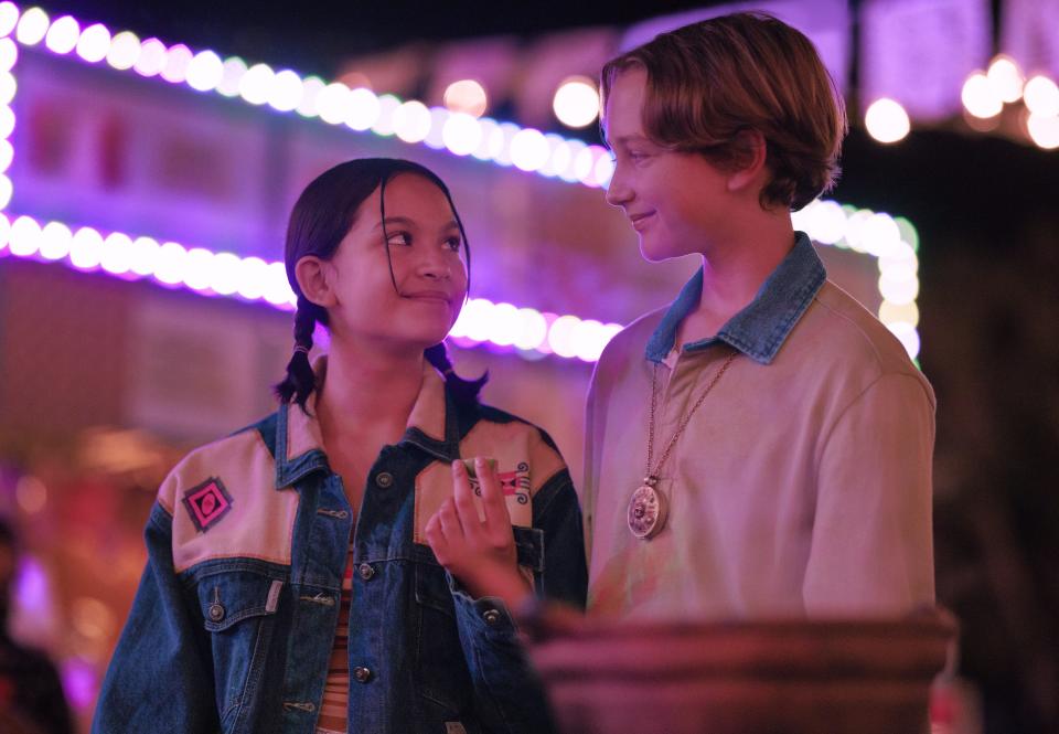 jodie and magda in the chosen one, standing at a carnival and smiling at each other with bright lights behind them