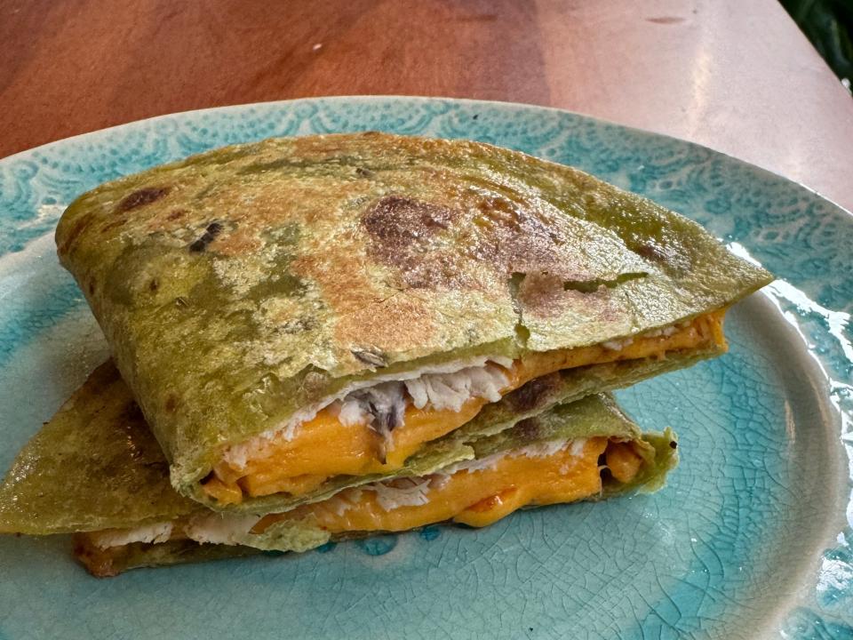 Quesadilla on green wrap filled with chicken and cheese cut in halves on a blue plate