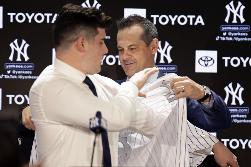 New York Yankees manager Aaron Boone, right, helps put a jersey on New York Yankees' Carlos Rodon during his introductory baseball news conference at Yankee Stadium, Thursday, Dec. 22, 2022, in New York. (AP Photo/Adam Hunger)