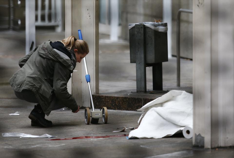 A police officer examines the crime scene next to a covered body following a shooting at the entrance of Building E of the courthouse in Frankfurt January 24, 2014. REUTERS/Ralph Orlowski (GERMANY - Tags: CRIME LAW TPX IMAGES OF THE DAY)