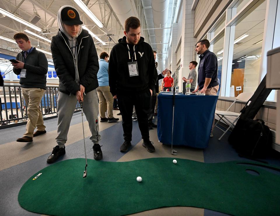 Freshman Zack Kingsbury tries a putt at the MassGolf table with fellow Northbridge High School student (and senior) Adam Minior during the Worcester Sports Management Summit at Worcester State University.