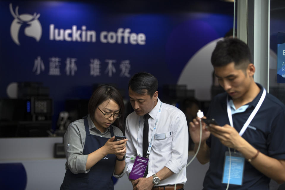 In this Aug. 15, 2018, photo, an employee helps a customer place an order on his smartphone at a Luckin Coffee pop-up shop at the World Robot Conference in Beijing. Shares of Luckin Coffee, a fast-growing rival to Starbucks in China, rose 20% in their U.S. stock market debut Friday, May 17, 2019. (AP Photo/Mark Schiefelbein)