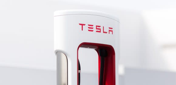 The top of a Tesla Supercharger, a white object shaped somewhat like a sleek gas pump, with Tesla's logo visible in red.