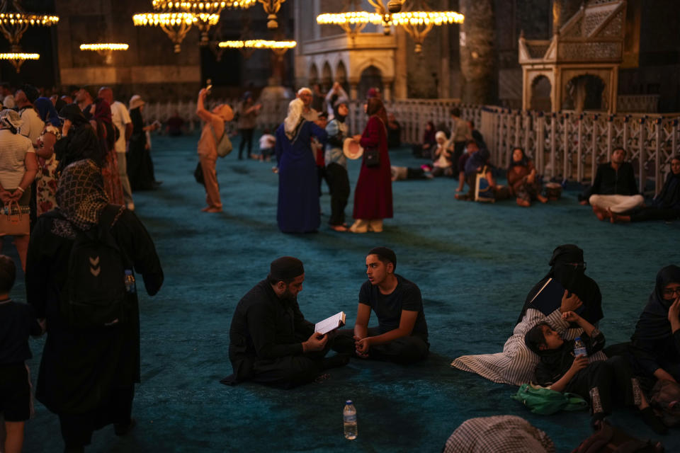 Muslim worshippers, center, read the Quran, Muslim's holiest book, as tourists and locals visit Byzantine-era Hagia Sophia mosque in Istanbul, Turkey, Tuesday, July 4, 2023. With tourism reaching or surpassing pre-pandemic levels across Southern Europe this summer, iconic sacred sites struggle to find ways to accommodate both the faithful who come to pray and millions of increasingly secular visitors attracted by art and architecture. (AP Photo/Francisco Seco)