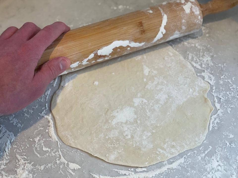 rolling out a piece of dough into a large circle with a rolling pin