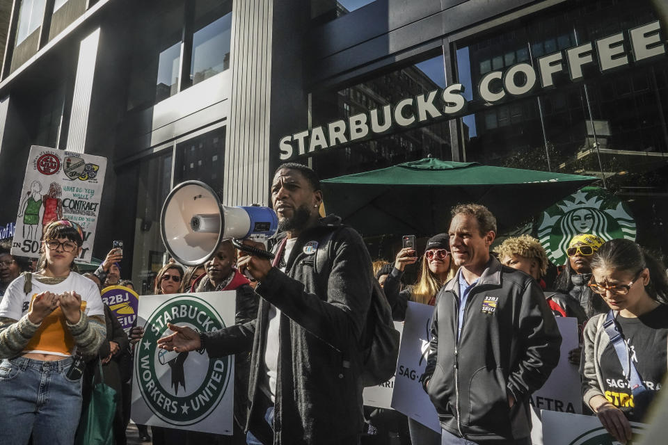 New York Public Advocate Jumaane Williams, center, uses a megaphone to address a coalition of unions and supporters of Starbucks workers, during a rally outside a midtown Manhattan Starbucks coffee store, calling for "fair schedules and wages," Thursday, Nov. 16, 2023, in New York. (AP Photo/Bebeto Matthews)