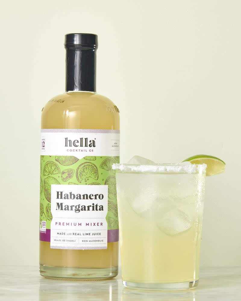 photo of Hella Habanero Margarita mix bottle with a mixed drink next to it on a marble surface with a light green background