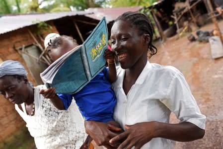 Mariatu Sesay, 15, smiles as she carries her daughter Nadia while she walks outside her house in the countryside village of Sierra