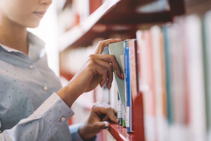 Rows of books on shelves with woman picking one out