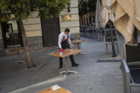 Waiter Miguel Santana disinfects a table prior opening a bar terrace in downtown Madrid, Spain, Wednesday, Sept. 30, 2020. The Spanish capital and its suburbs, the region in Europe where a second coronavirus wave is expanding by far the fastest, are edging closer to stricter mobility curbs and limits on social gatherings after days of a political row that has angered many Spaniards. (AP Photo/Bernat Armangue)